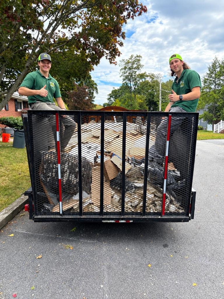 Patrick and Joey from P & J Junk Removal giving thumbs up in front of their loaded trailer